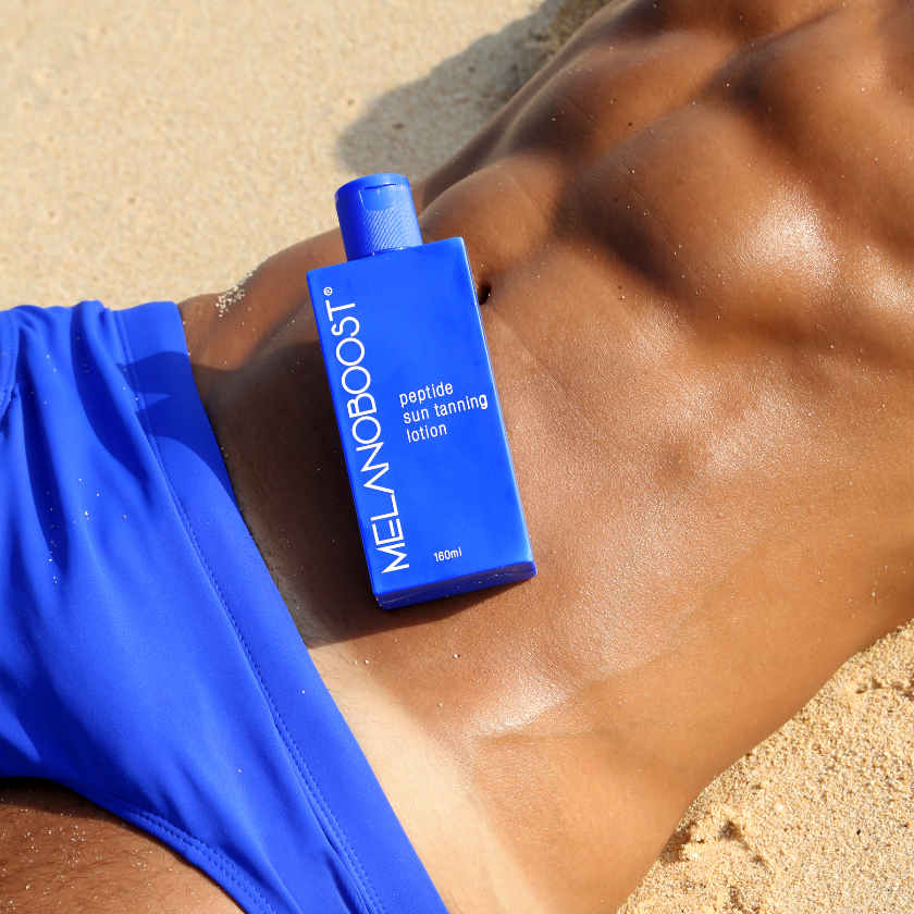 tanned_man_in_blue_swim_trunks_lying_on_Beach_showing_tanline_with_Melanoboost_Peptide_Sun_Tan_Accelerator_Lotion