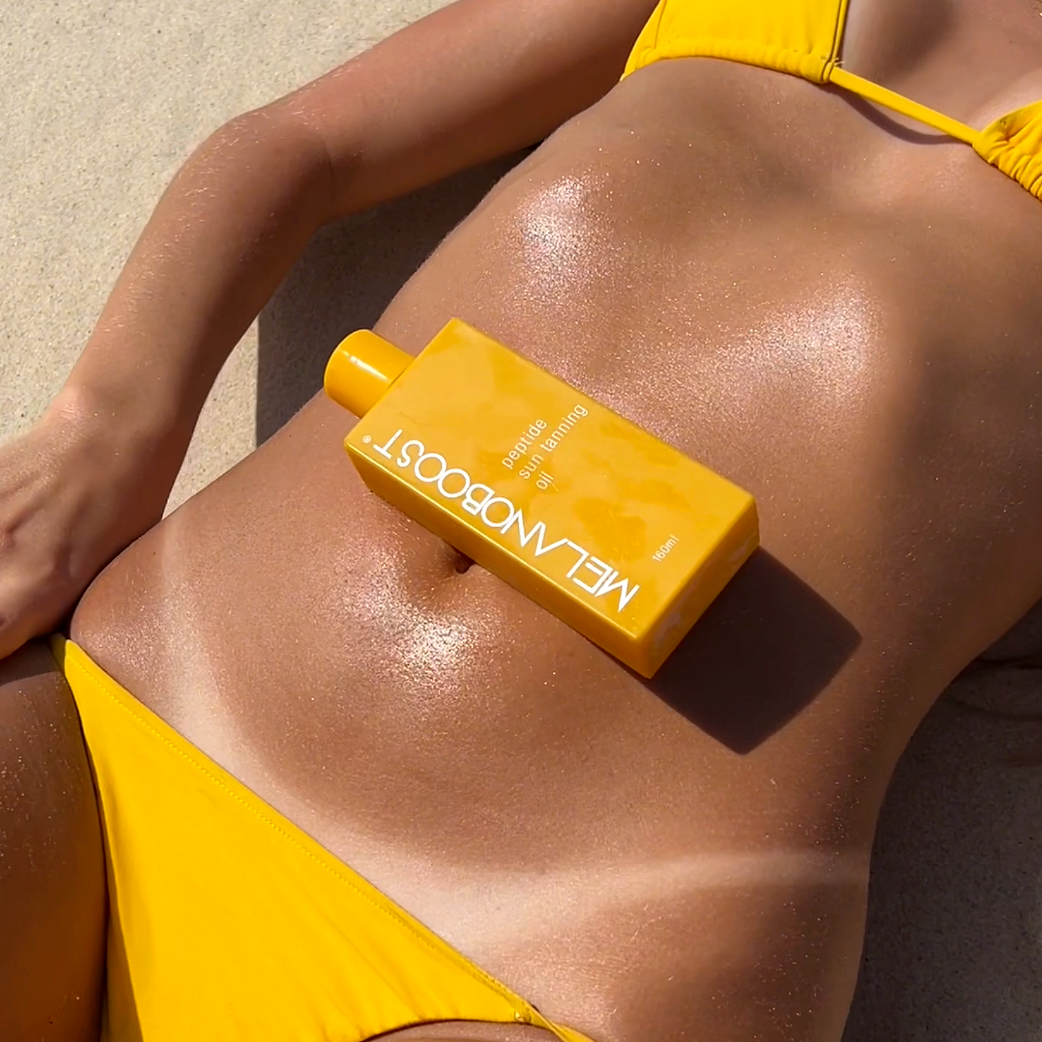 Girl_lying_on_beach_in_yellow_Bikini_with_tanlines_and_bottle_of_Melanoboost_Peptide_Sun_Tan_Accelerator_Oil