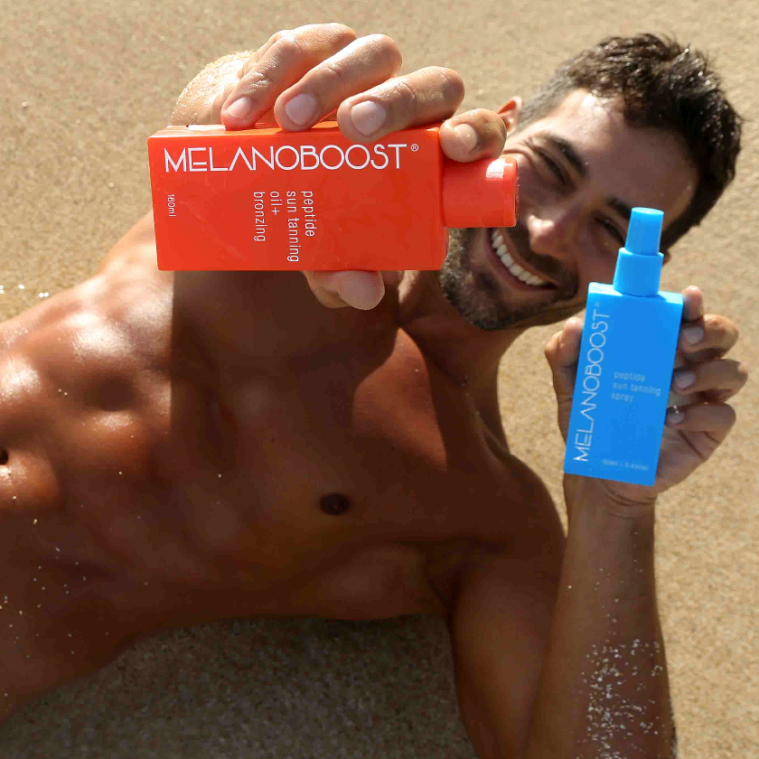 man_lying_on_sandy_beach_holding_Melanoboost_Peptide_Sun_Tanning_Oil_and_Spray
